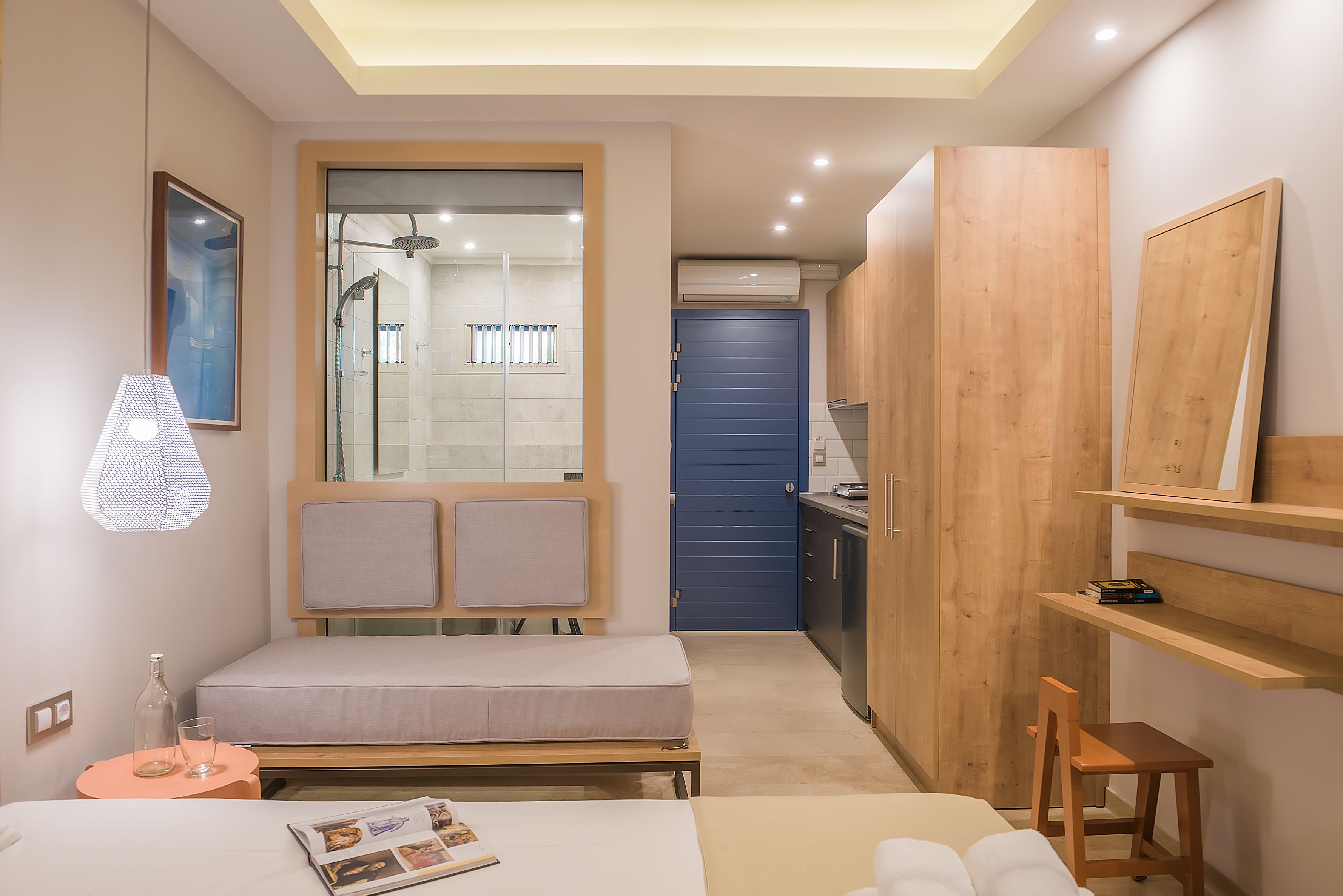 A compact hotel room with a bed, bedside table, and a small seating area.