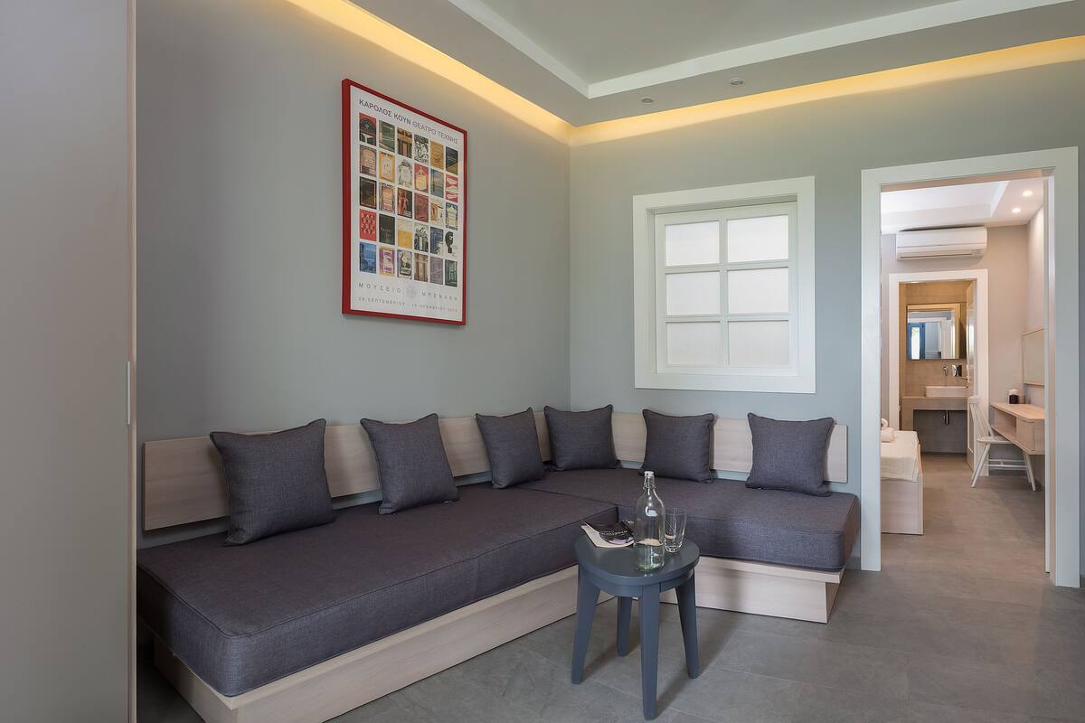 A modern living room with a sectional sofa, a small table with a bottle and glasses, and a framed photo on the wall.