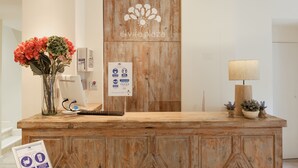 A wooden reception desk with a logo, a computer, a vase with flowers, and a lamp. - Hotel Boutique Elvira Plaza (Seville)
