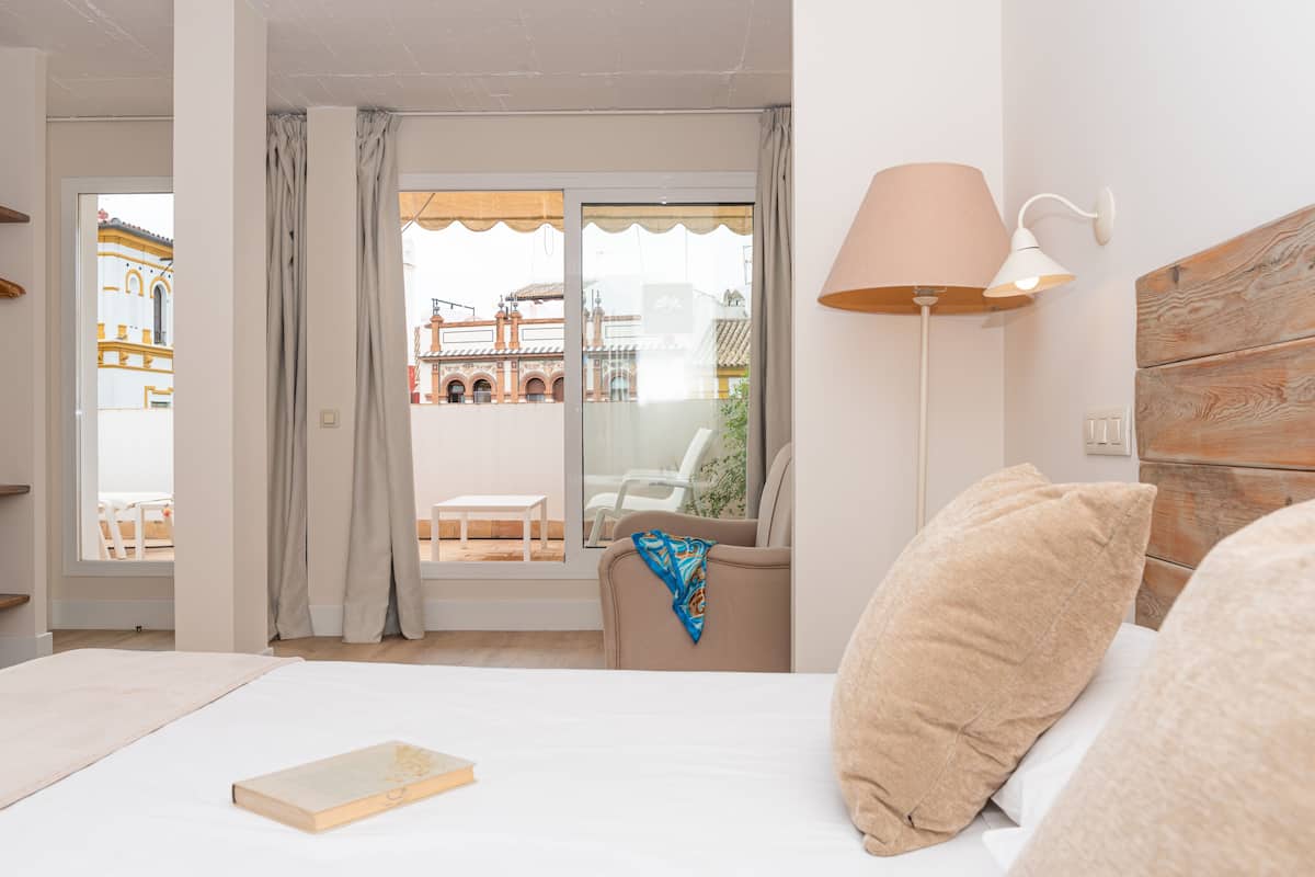 A hotel room with a bed, a reading lamp, a window with curtains, and a view of a building outside.