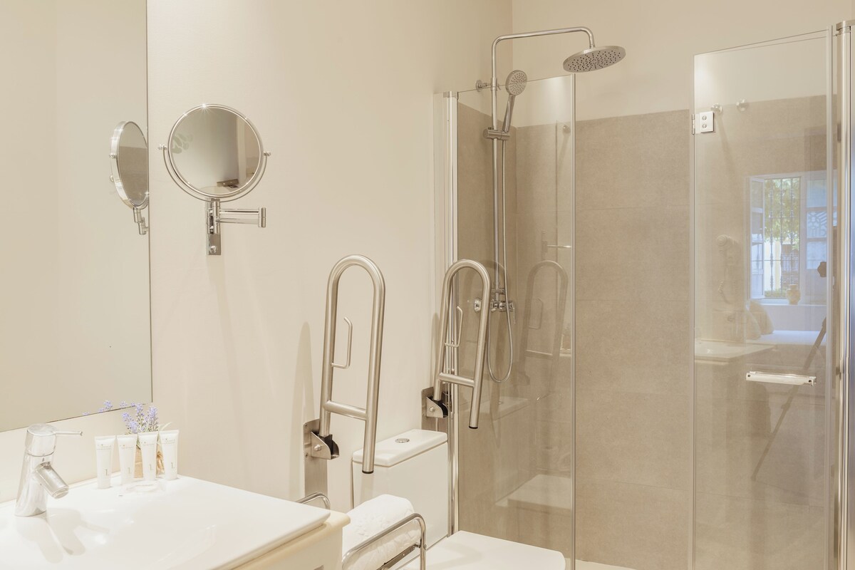 Un baño moderno con ducha de vidrio, tocador con espejo y lavamanos con artículos de aseo.