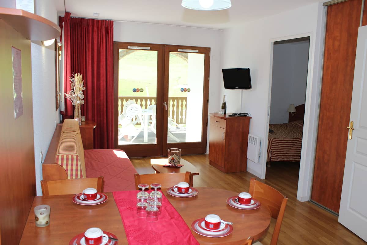 A dining area with a wooden table set for four, a red table runner, and a view of the outside through a sliding glass door.