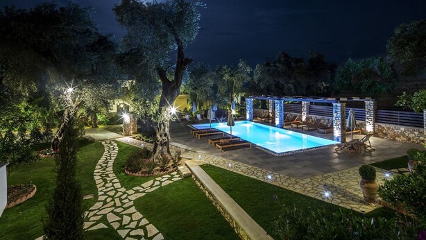 A nighttime outdoor pool area with a stone pathway, lounge chairs, and a pergola. - Vassilis Guest House (Parga)