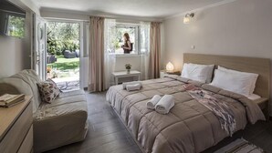 A bedroom with a large bed, a bedside table, a nightstand, a window with curtains, and a view of the outdoors. - Vassilis Guest House (Parga)