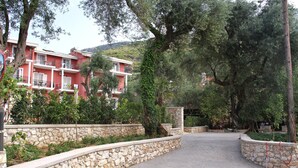 A paved pathway leading to a building with balconies, surrounded by stone walls and greenery. - Vassilis Guest House (Parga)
