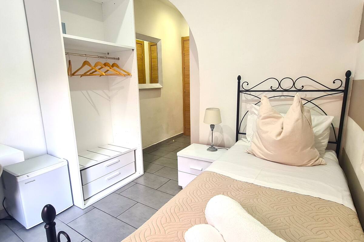 Une chambre à coucher comprenant un lit, une table de chevet, une lampe et une armoire avec des cintres.