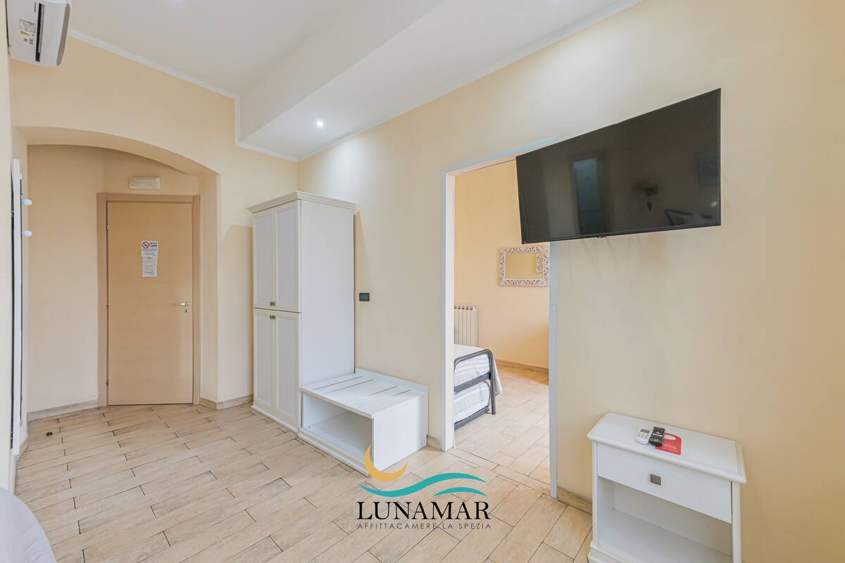 Un appartement moderne avec un plancher en bois, une armoire blanche, un téléviseur fixé au mur et une petite table de chevet.