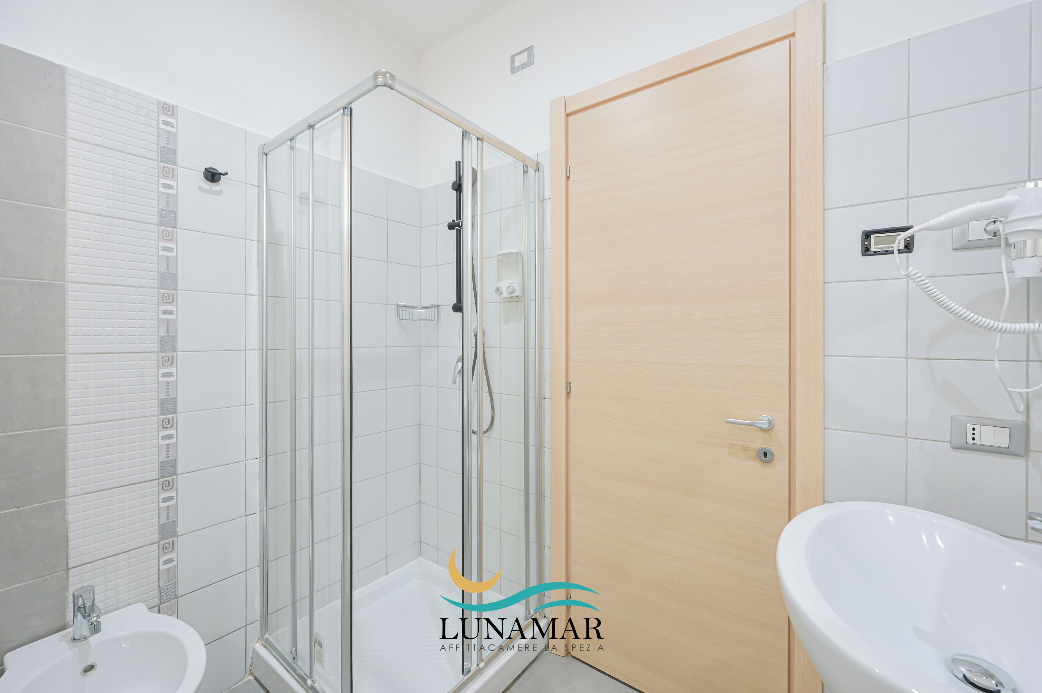 A modern bathroom with a glass-enclosed shower, a wooden door, and a white sink.