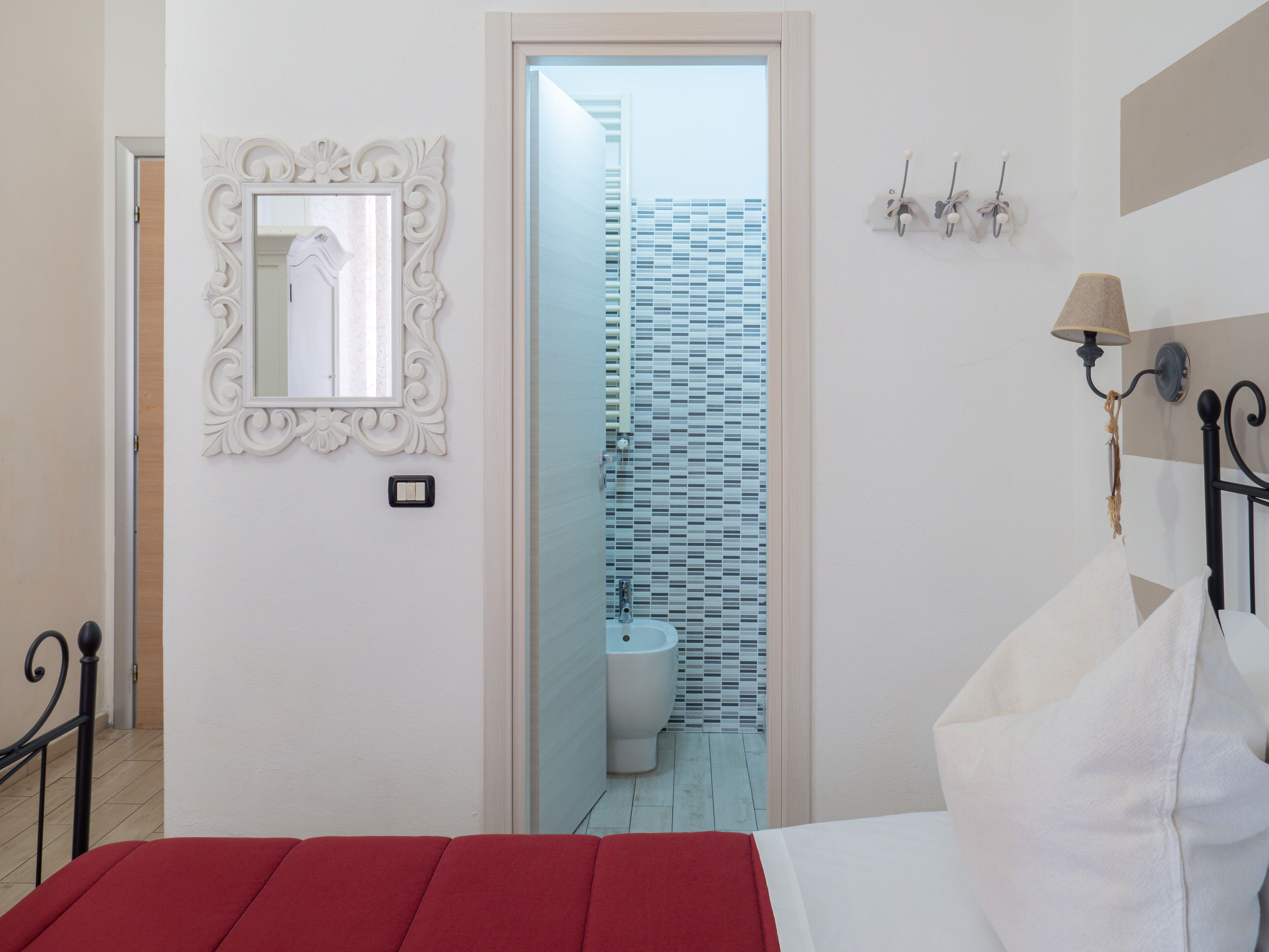 Quarto com cama, espelho, luminária e vista para o banheiro.