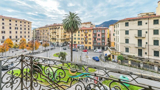 A cityscape with multi-story buildings, a roundabout, and a palm tree. - Affittacamere Lunamar (La Spezia)