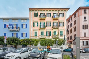 Un edificio de varios pisos con balcones, coches aparcados y cielo despejado.
