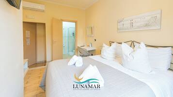 A hotel room with a bed, a desk, a chair, a shower area, and a painting on the wall.