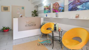 A reception area with a desk, two yellow chairs, and artwork on the walls. - Affittacamere Lunamar (La Spezia)