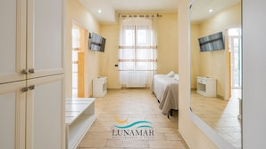 A bedroom with a bed, a TV, a window with curtains, and a mirror. - Affittacamere Lunamar (La Spezia)