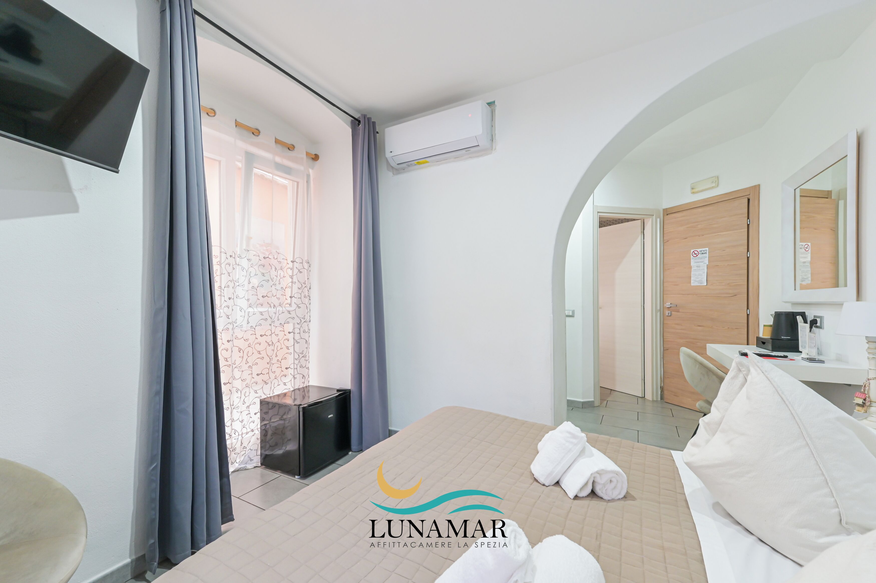Een hotelkamer met een bed, een televisie, een airconditioningapparaat, een badkamer met een spiegel en een deur.