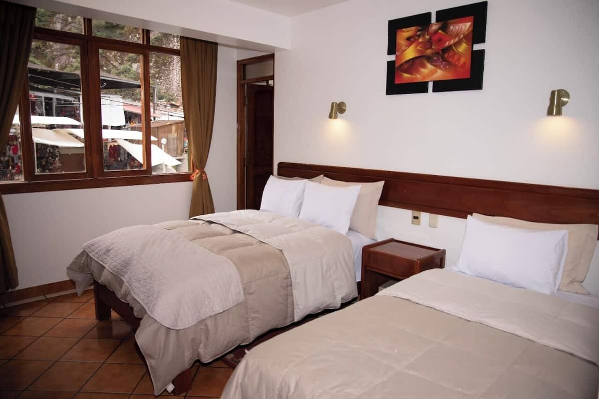 A hotel room with two beds, a window with curtains, a wall-mounted light, and a painting.