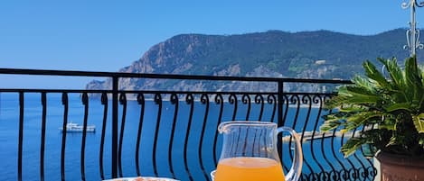 Een ontbijttafel met gerechten zoals wafels, croissants en fruit, met een prachtig uitzicht op zee en bergen op de achtergrond.