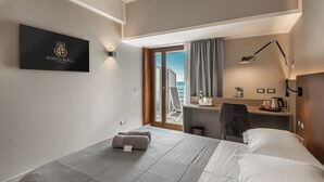 A hotel room with a bed, a desk with a chair, a minibar, a view of the sea, and a logo on the wall. - Hotel Porto Roca (Monterosso al Mare)