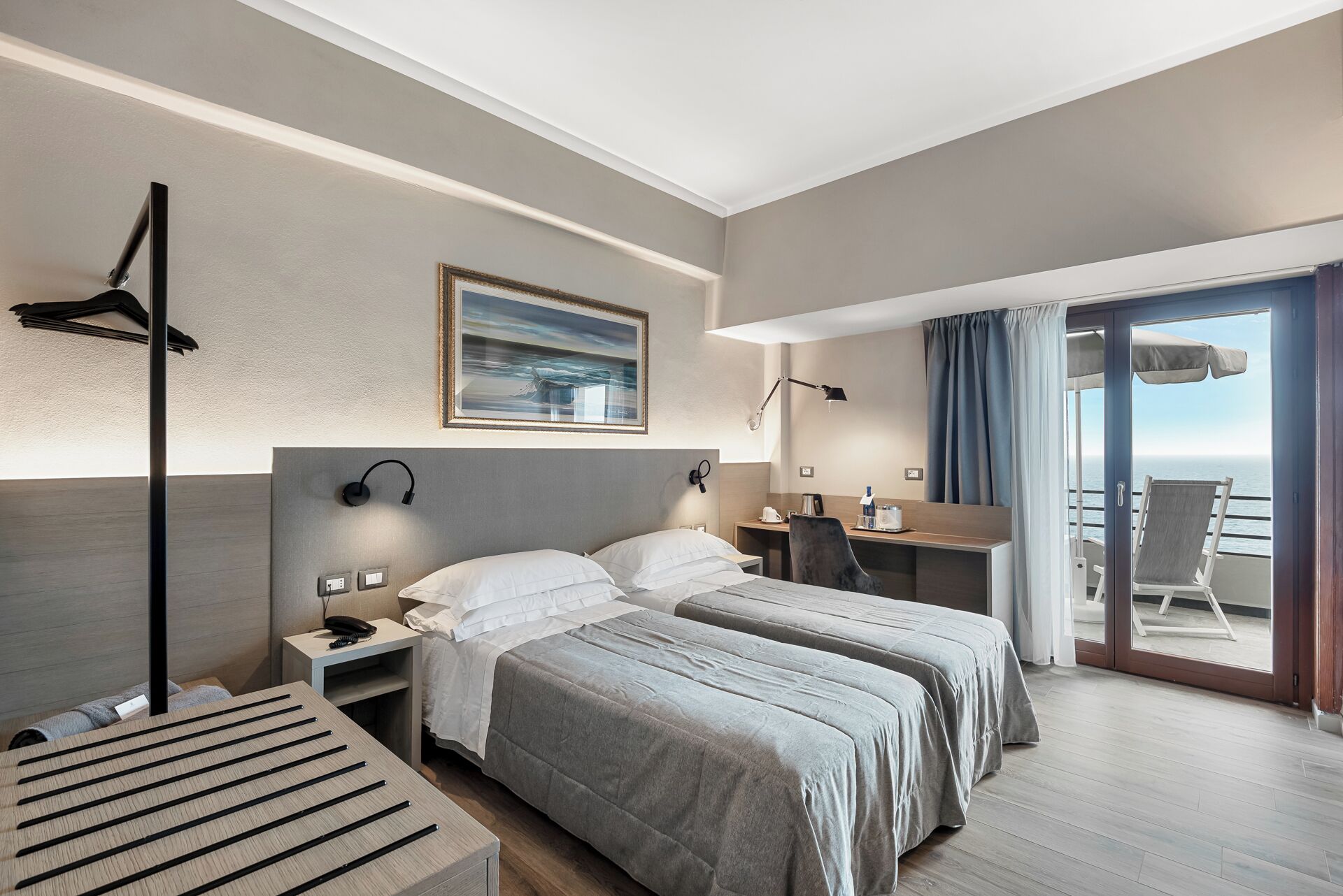 A hotel room with two beds, a desk, a chair, a desk lamp, a phone, and a painting on the wall.