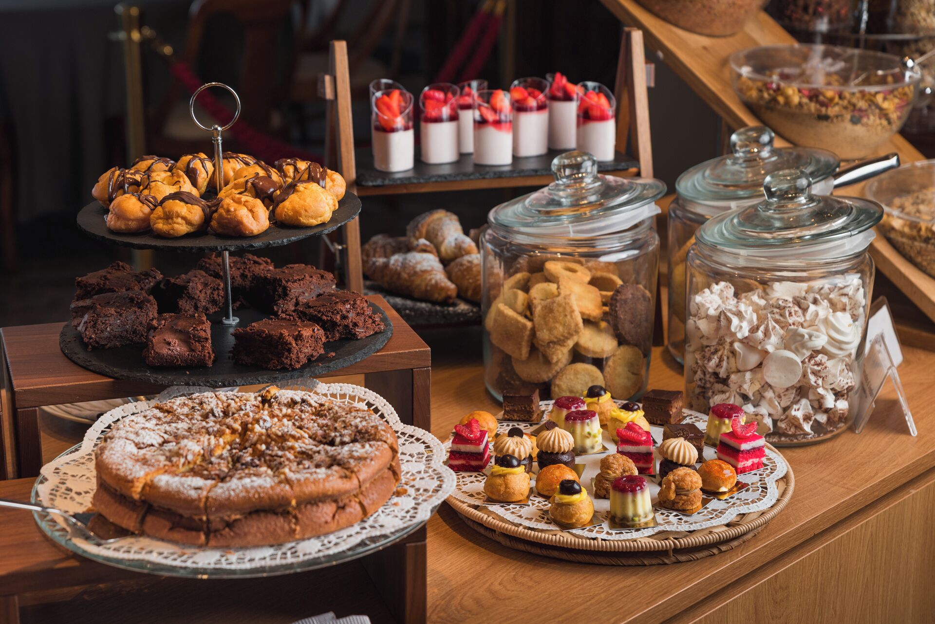 Une variété de desserts et de pâtisseries étaient exposés, notamment un présentoir à gâteaux à plusieurs étages, des bocaux remplis de biscuits et un grand gâteau posé sur un chemin de table en dentelle.