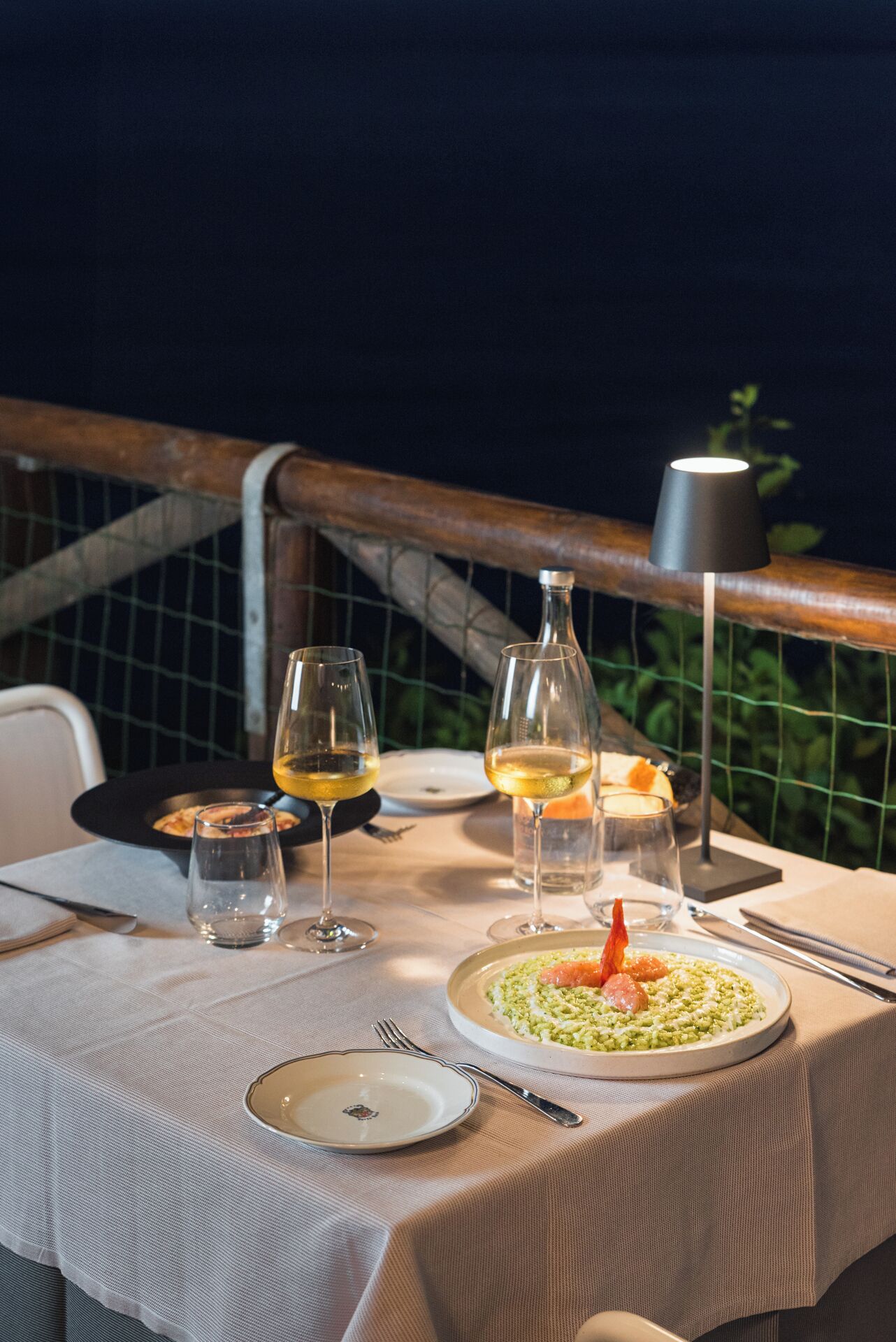 A table set for a meal with wine glasses, a bottle, and a plate of food.