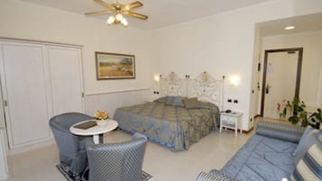 A bedroom with a bed, a sofa, a chair, a small table, and a ceiling fan.