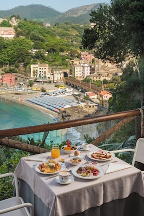 A table set with breakfast on a balcony overlooking a coastal town and beach. - Hotel Porto Roca (Monterosso al Mare)