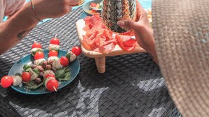 A poolside dining area with a table set for two, featuring a plate of caprese skewers, a pineapple with a drink, and a tray of watermelon slices. - Hotel Porto Roca (Monterosso al Mare)
