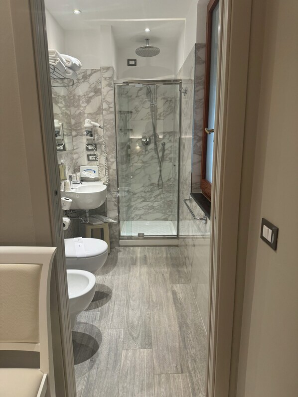 A modern bathroom with a glass-enclosed shower, marble walls, and a wooden floor. - Hotel Porto Roca (Monterosso al Mare)