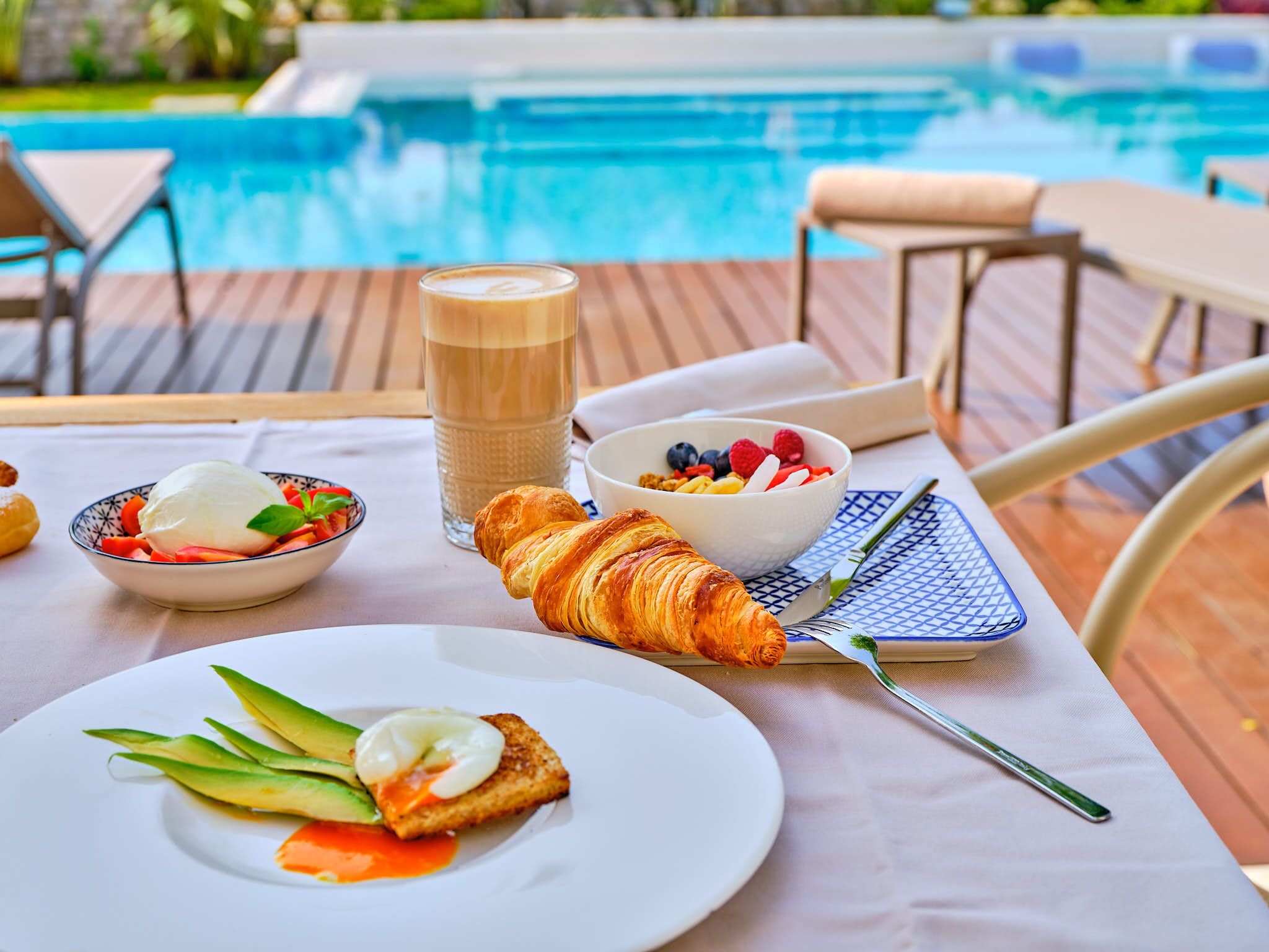 Ontbijt bij het zwembad, met croissants, fruit en koffie.