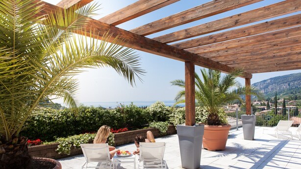 A covered outdoor seating area with a view of the sea, surrounded by potted plants and a wooden pergola. - Tobago Hotel (Garda)