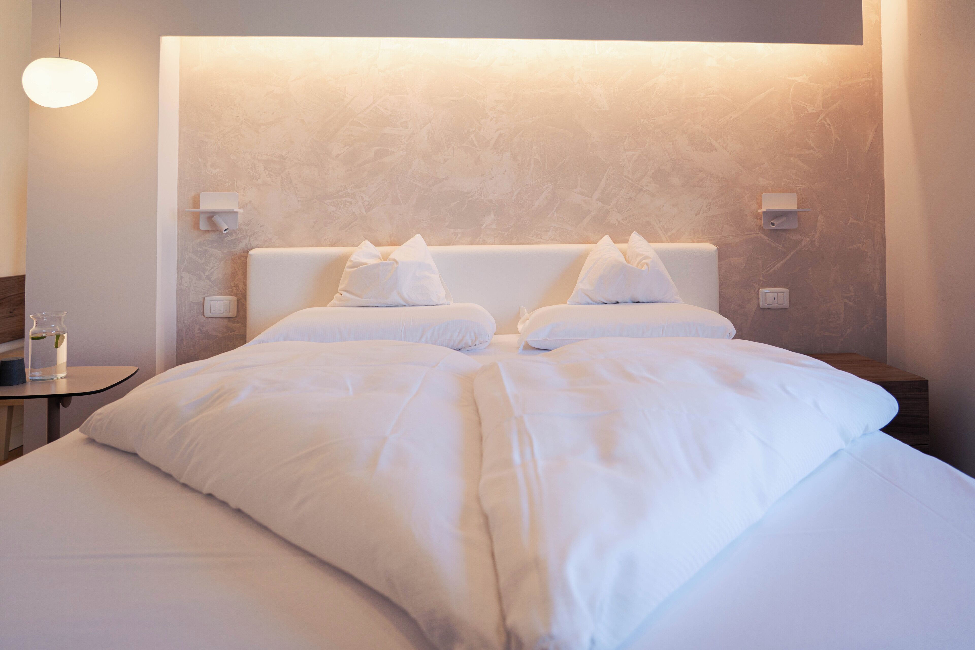 Un lit double bien fait, avec du linge de lit blanc, une tête de lit à motifs de marbre et des lampes de chevet.