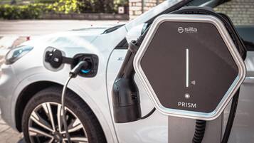 Un vehículo eléctrico blanco cargándose en una estación identificada como "Silla Industries PRISM".