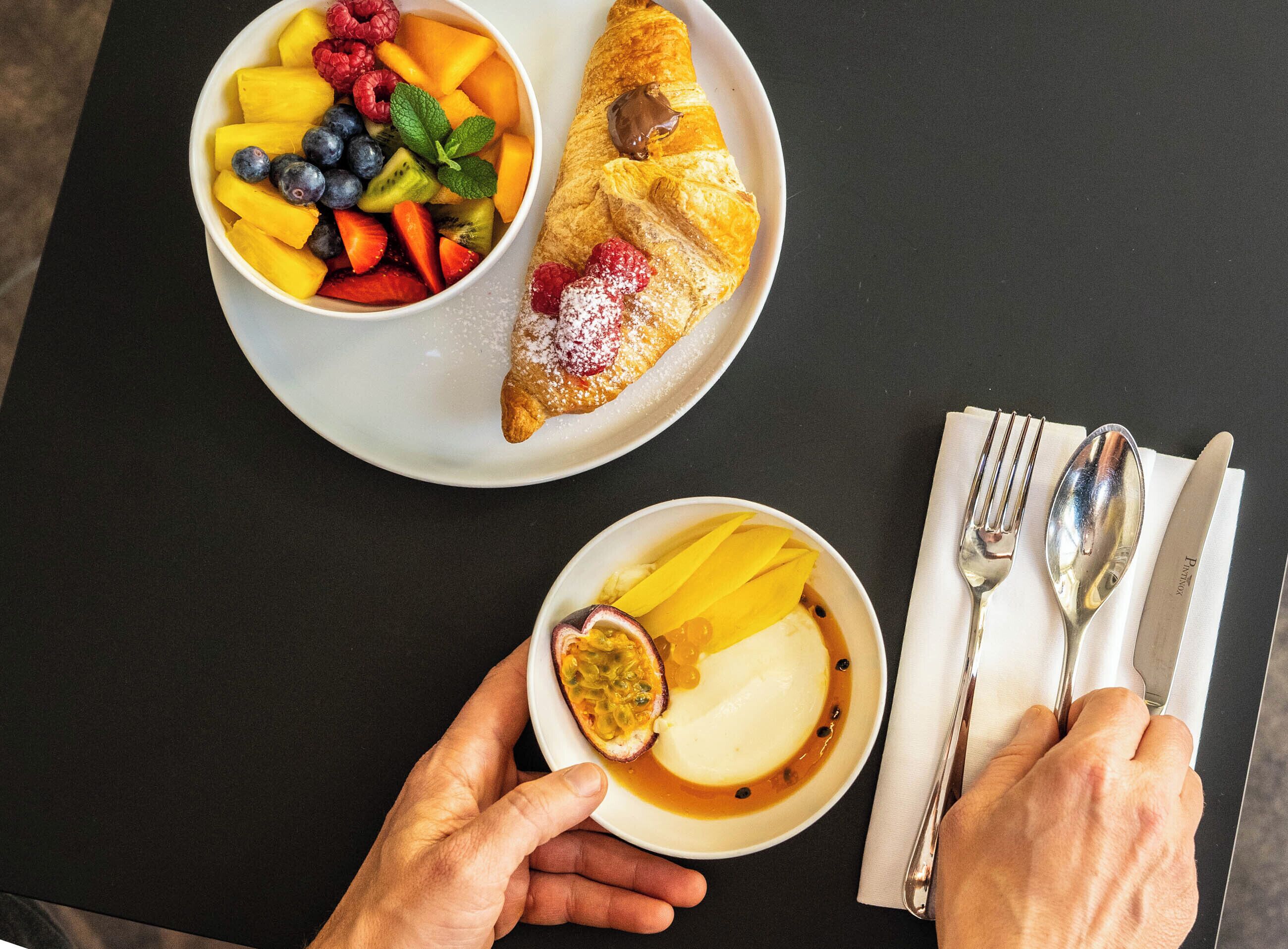 A table with a plate of fruit, a pastry, and a bowl of dessert.