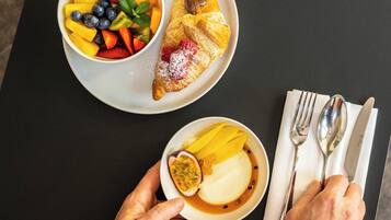 A table with a plate of fruit, a pastry, and a bowl of dessert.