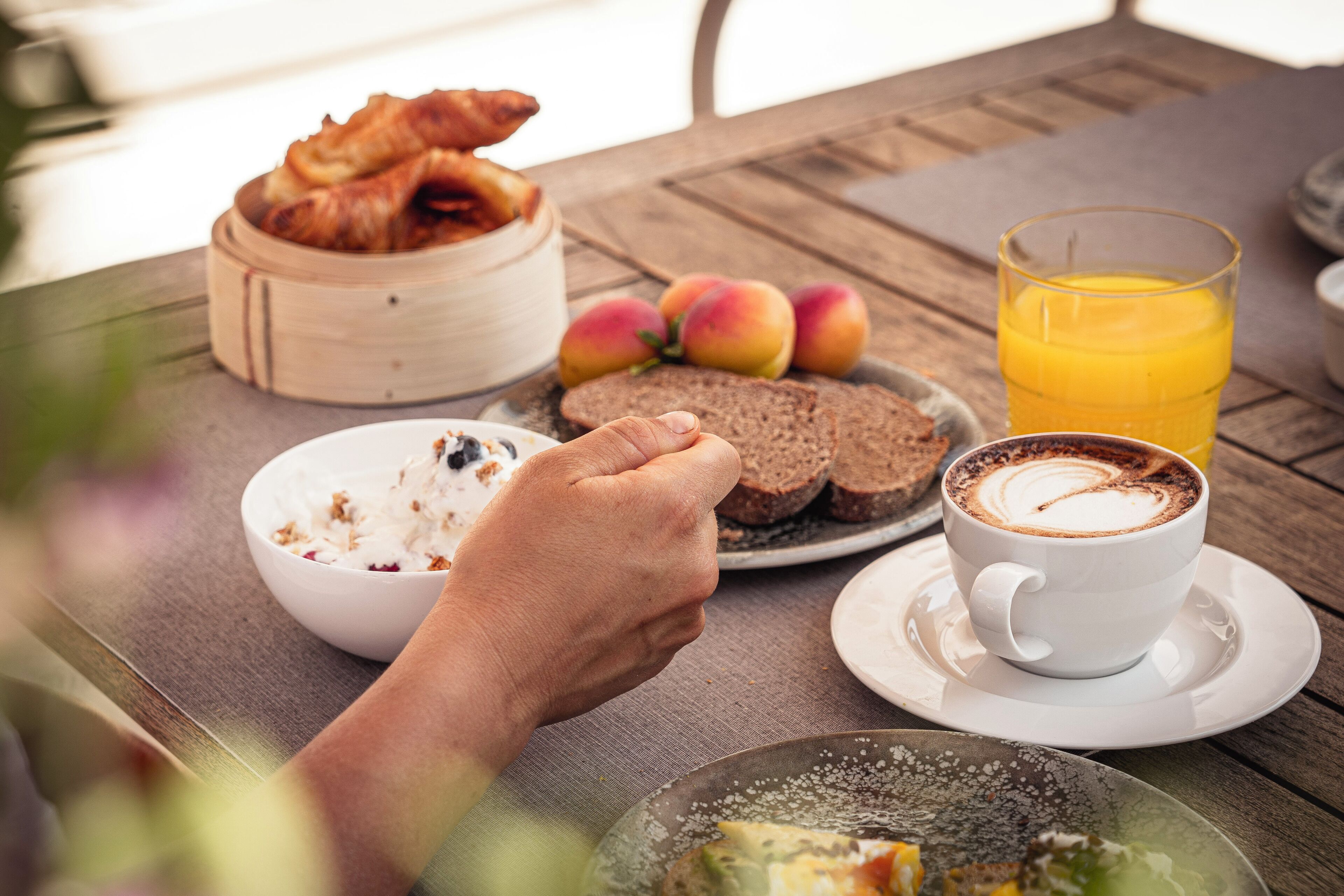 Una mesa de desayuno con cruasanes, un tazón de cereal, un plato de pan, un vaso de jugo de naranja y una taza de café.