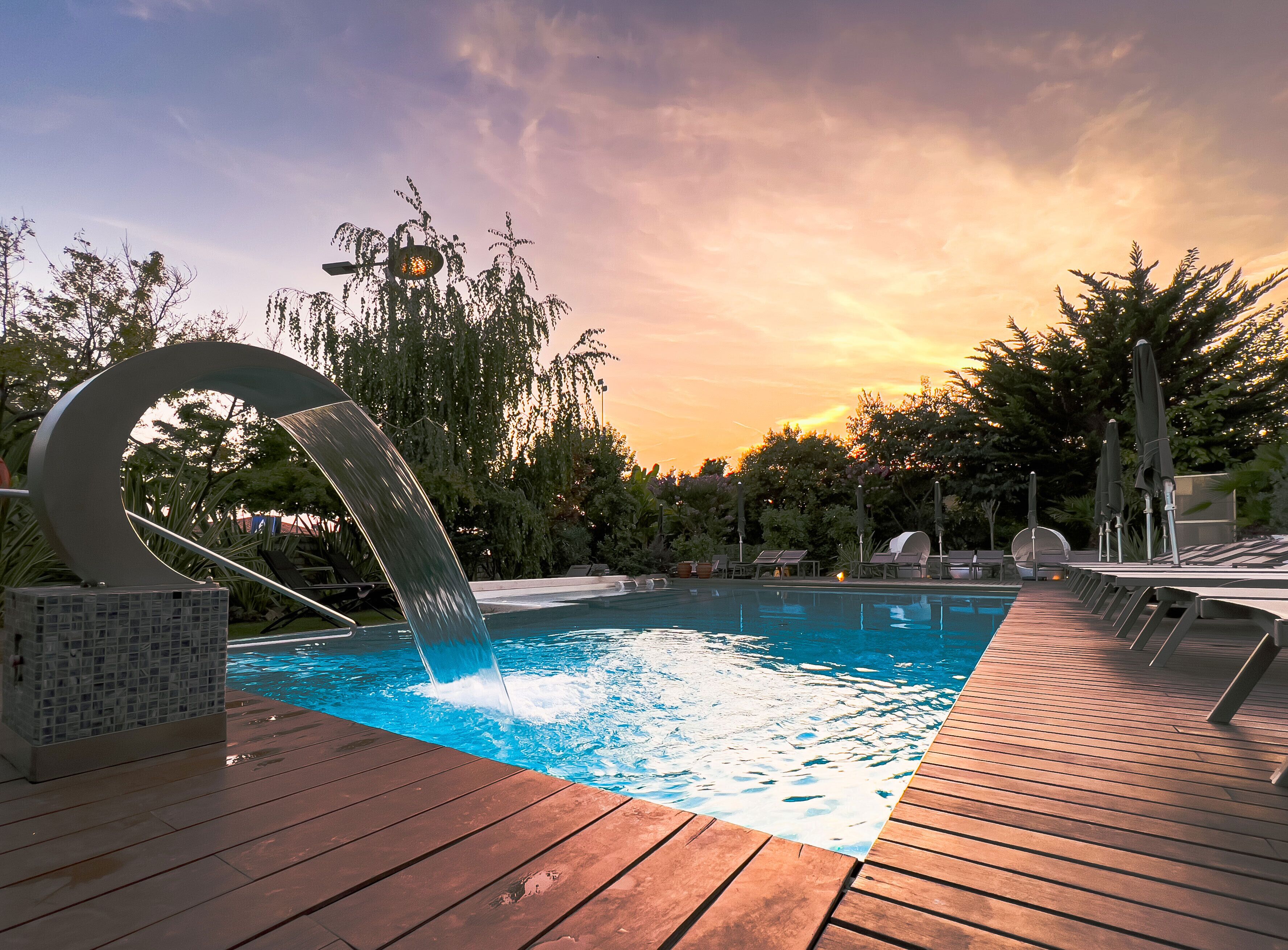 Ein Pool mit einem kreisförmigen Wasserspiel, umgeben von Holzterrasse und Liegestühlen.