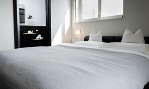 A hotel room with a large bed, a black headboard, a nightstand with a lamp, a mirror, and a window with a view of the sky. - Tobago Hotel (Garda)
