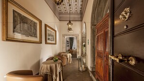 A hallway with tables and chairs, a wooden door, and framed artwork on the walls. - Dimora degli Dei (Rome)