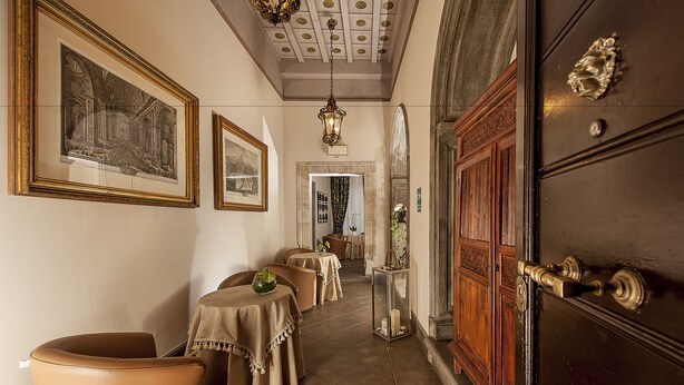 A hallway with tables and chairs, a wooden door, and framed artwork on the walls. - Dimora degli Dei (Rome)