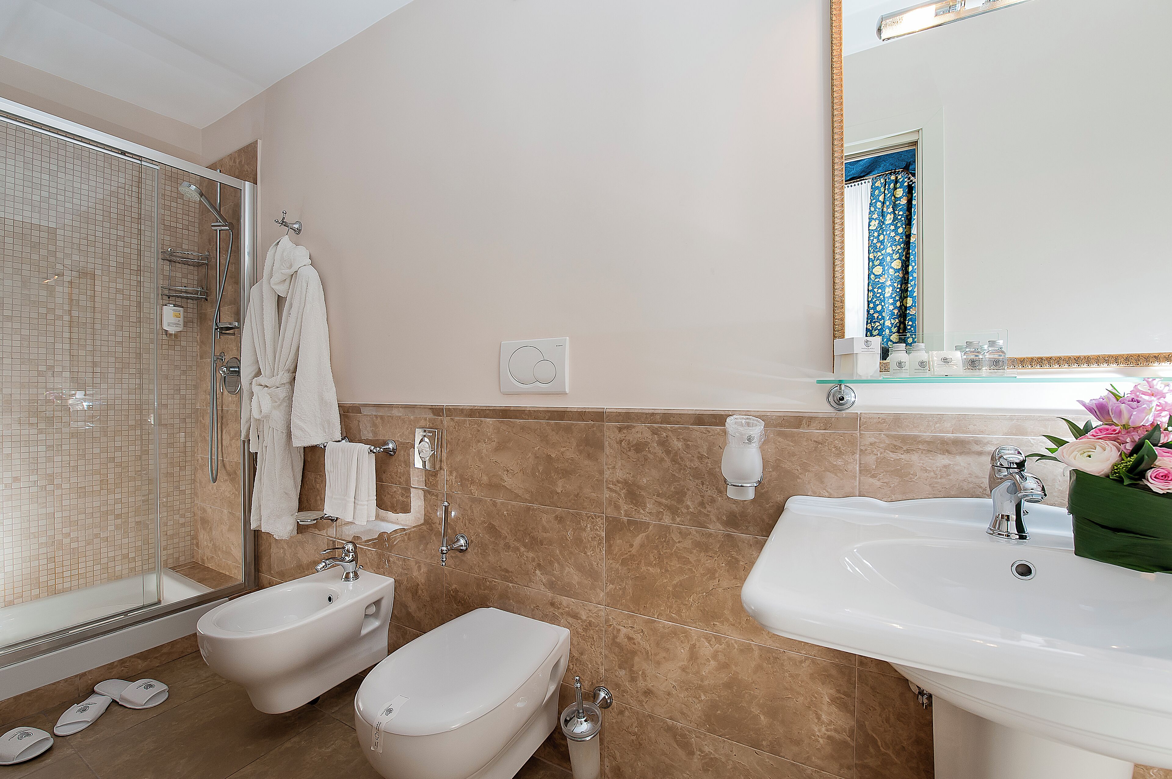 A modern bathroom with a glass-enclosed shower, a bidet, a sink, and a mirror with a decorative frame.