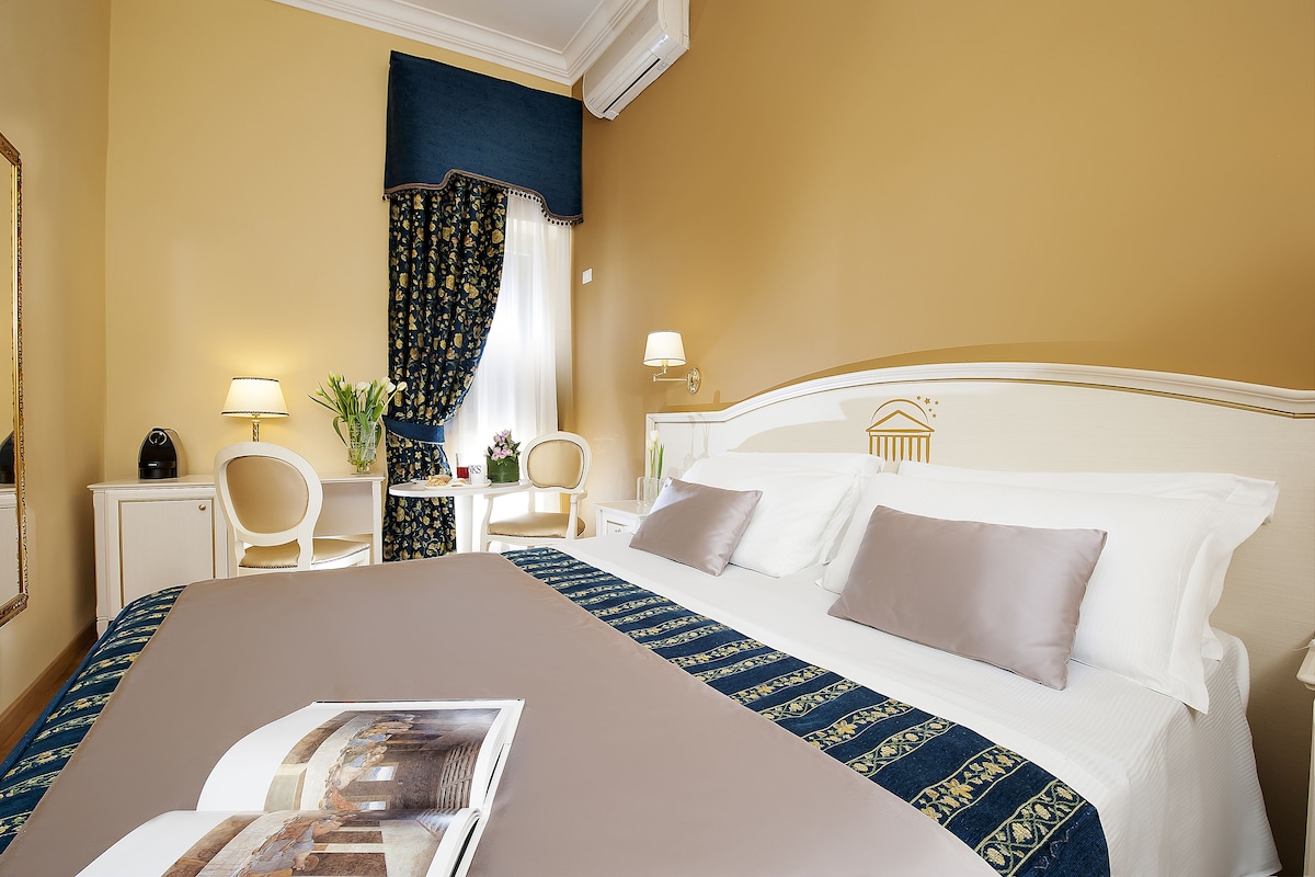 A hotel room with a large bed, a desk with a chair, a lamp, and a window with curtains.