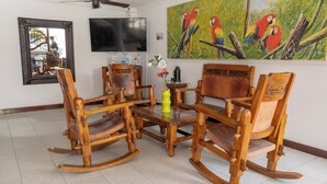 Uma sala de estar com poltronas de balanço de madeira, uma mesa de centro e uma televisão fixada na parede.