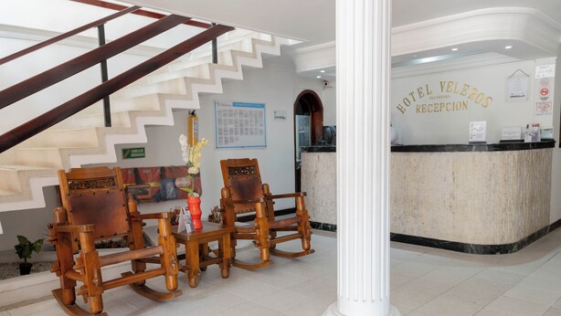 Uma área de recepção de hotel com escada, cadeiras de balanço de madeira e balcão de recepção.