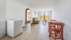 A compact living space with a kitchenette, a dining area with wooden furniture, a sofa, and a view through a window. - Hotel Alicante (Bogotá)