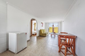 Ein kompakter Wohnbereich mit Küchenzeile, einem Essbereich mit Holzmöbeln, einer Couch und Blick durch ein Fenster.