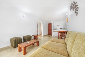 A living room with a sofa, ottomans, a coffee table, and a kitchen area in the background. - Hotel Alicante (Bogotá)