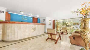 A reception area with a blue wall, a reception desk, and a seating area with chairs and a sofa. - Hotel Alicante (Bogotá)
