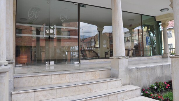 A hotel entrance with a glass facade, steps leading up to the entrance, and a visible address sign. - Hotel Alicante (Bogotá)