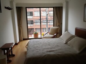 A hotel room with a bed, a chair, a small table, and a window with curtains. - Hotel Alicante (Bogotá)
